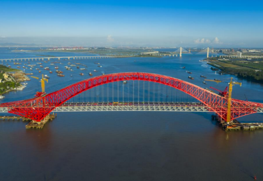 明珠灣大橋位于廣州市南沙區(qū)龍穴南水道之上，是粵港澳大灣區(qū)的重要連接通道。大橋工程全長約10.42公里，主線全長約9.1公里，主橋采用中承式六跨連續(xù)鋼桁拱橋，全長1016米，為同類型橋梁最大跨度。氣勢恢宏的明珠灣大橋綿延伸向遠(yuǎn)方，將南沙多條核心主干道緊緊連在一起，構(gòu)筑了明珠灣區(qū)內(nèi)部核心交通環(huán)，是廣州面向粵港澳大灣區(qū)建設(shè)的交通樞紐工程和地標(biāo)性建筑。圖為南沙明珠灣大橋。