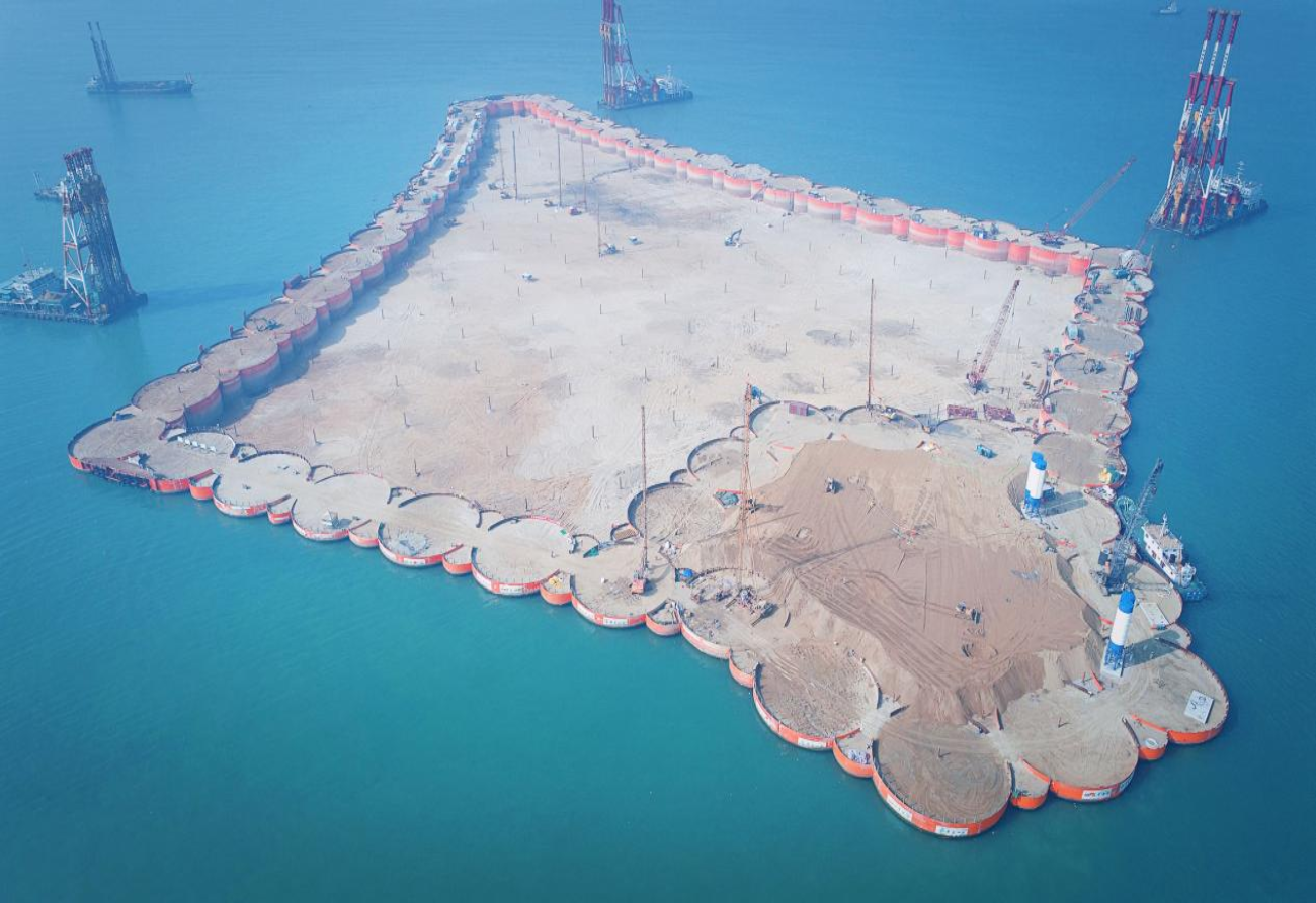 2016年12月28日，深中通道西人工島先行開建，這是深中通道工程在伶仃洋上落下的“第一子”，標(biāo)志著深中通道正式開工。西人工島島體采用菱形設(shè)計(jì)，形狀如同海上風(fēng)箏，是實(shí)現(xiàn)跨海橋梁和海底隧道轉(zhuǎn)換的關(guān)鍵。工程使用世界最大十二錘聯(lián)動液壓振動錘組，高精度振沉57個(gè)巨型鋼圓筒，歷時(shí)141天實(shí)現(xiàn)西人工島合龍，刷新了“外?？焖俪蓫u”施工紀(jì)錄。圖為深中通道西人工島海上施工現(xiàn)場。